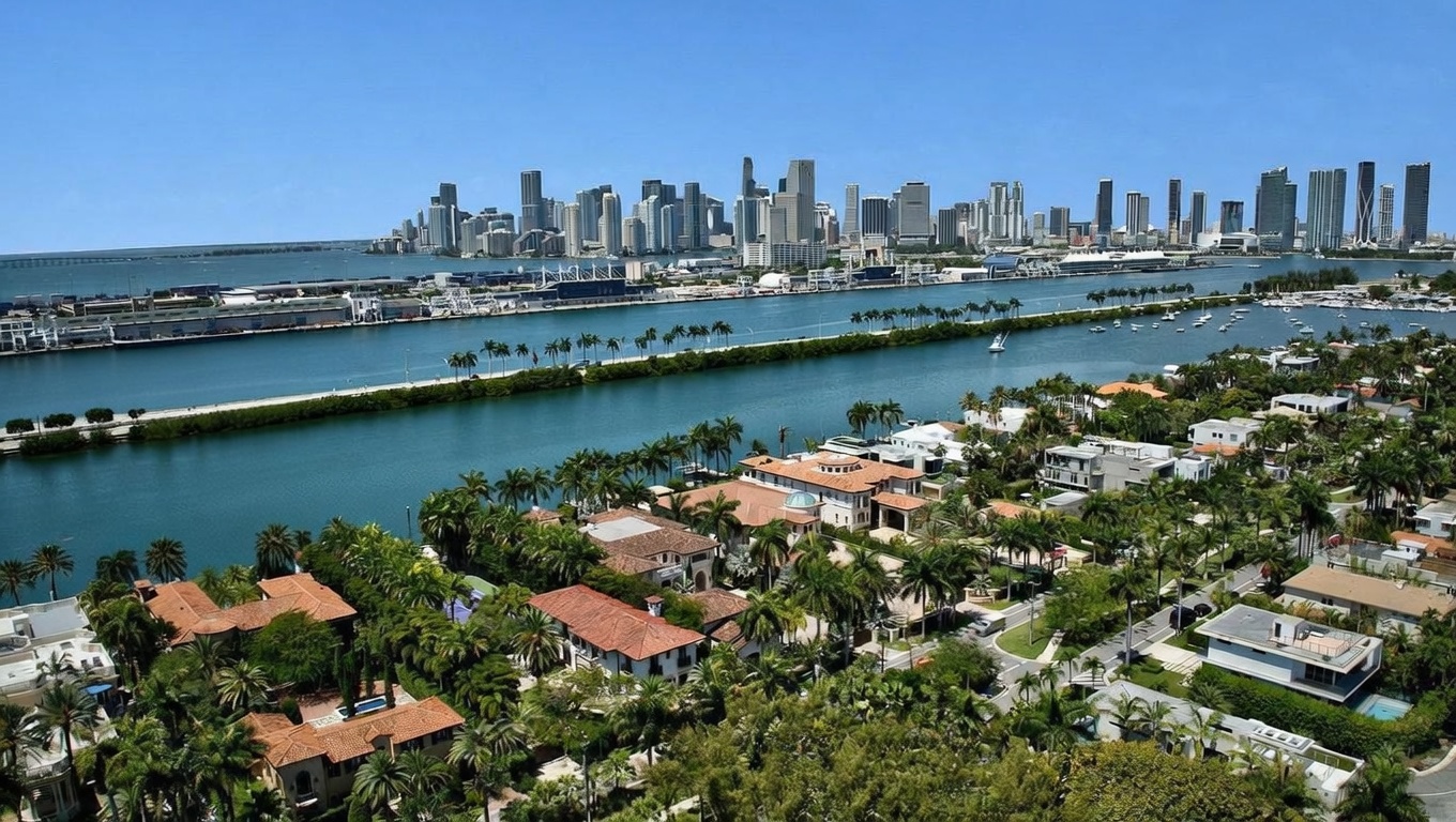 This aerial view showcases a luxurious waterfront neighborhood with stunning city skyline views. The scene features opulent homes with red-tiled roofs nestled among lush greenery and palm trees, bordering a tranquil waterway. The composition highlights the desirable location and upscale lifestyle associated with this real estate.