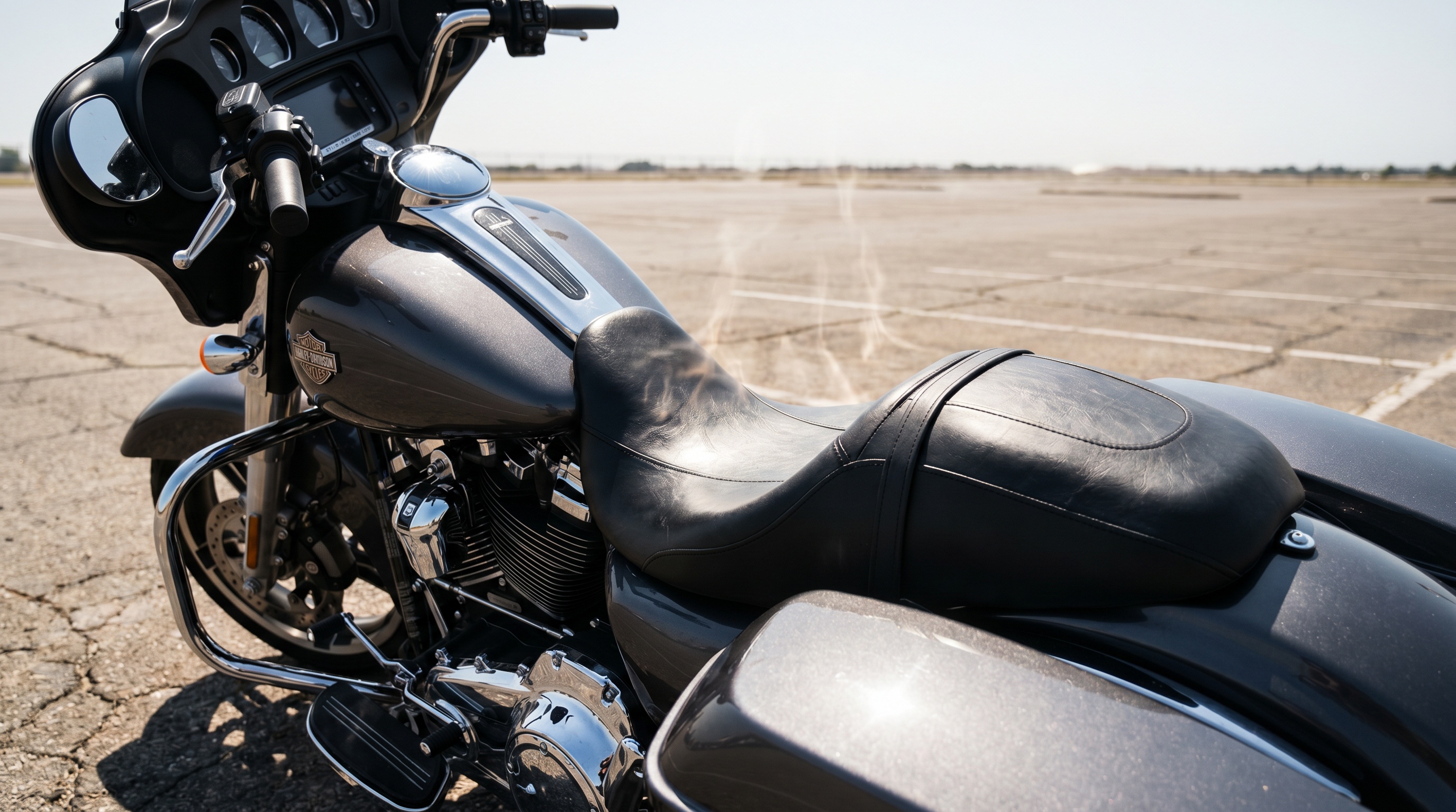 Close view of a stock black vinyl Harley Street Glide seat baking under direct summer sun on a hot asphalt parking lot