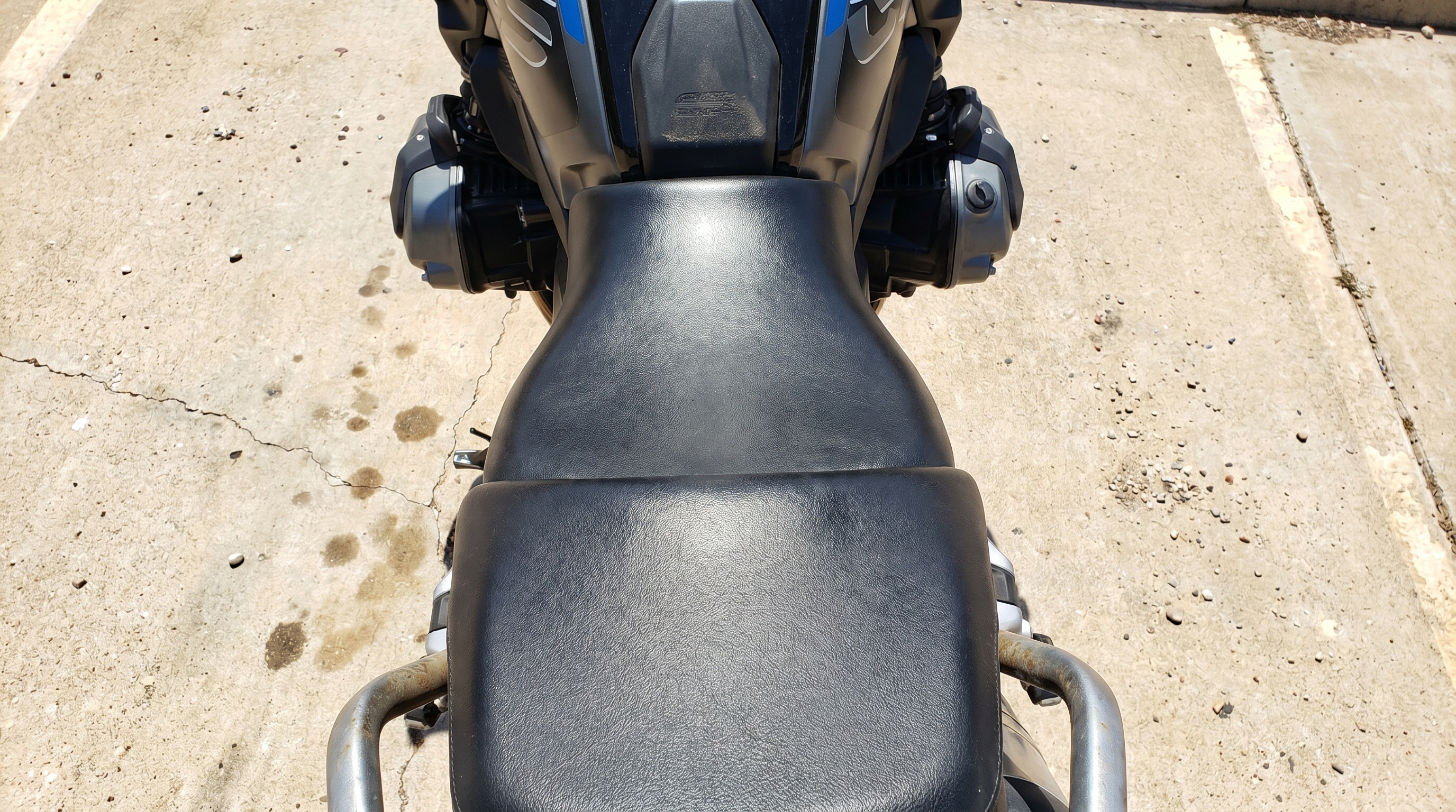 Close view of BMW R1250GS factory seat surface in direct midday sun showing heat buildup on black vinyl