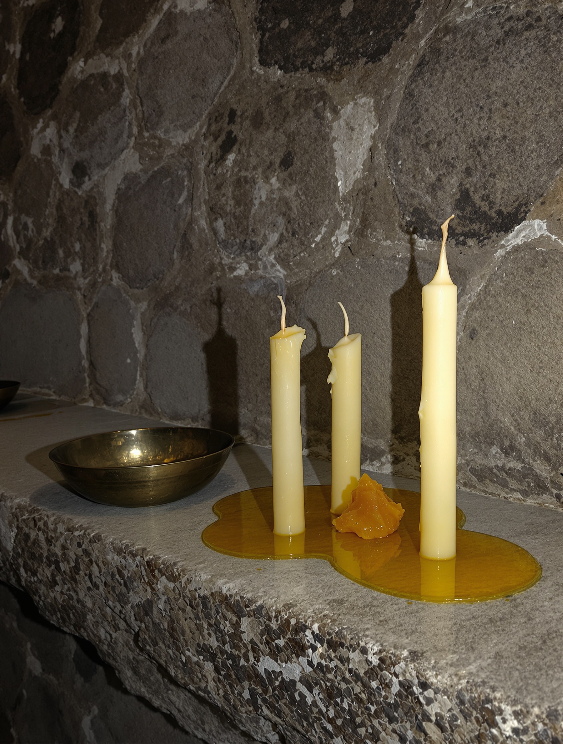 Snuffed beeswax candle stubs and raw resin on a limestone ledge for Diamonitirion Elixir Atonit.