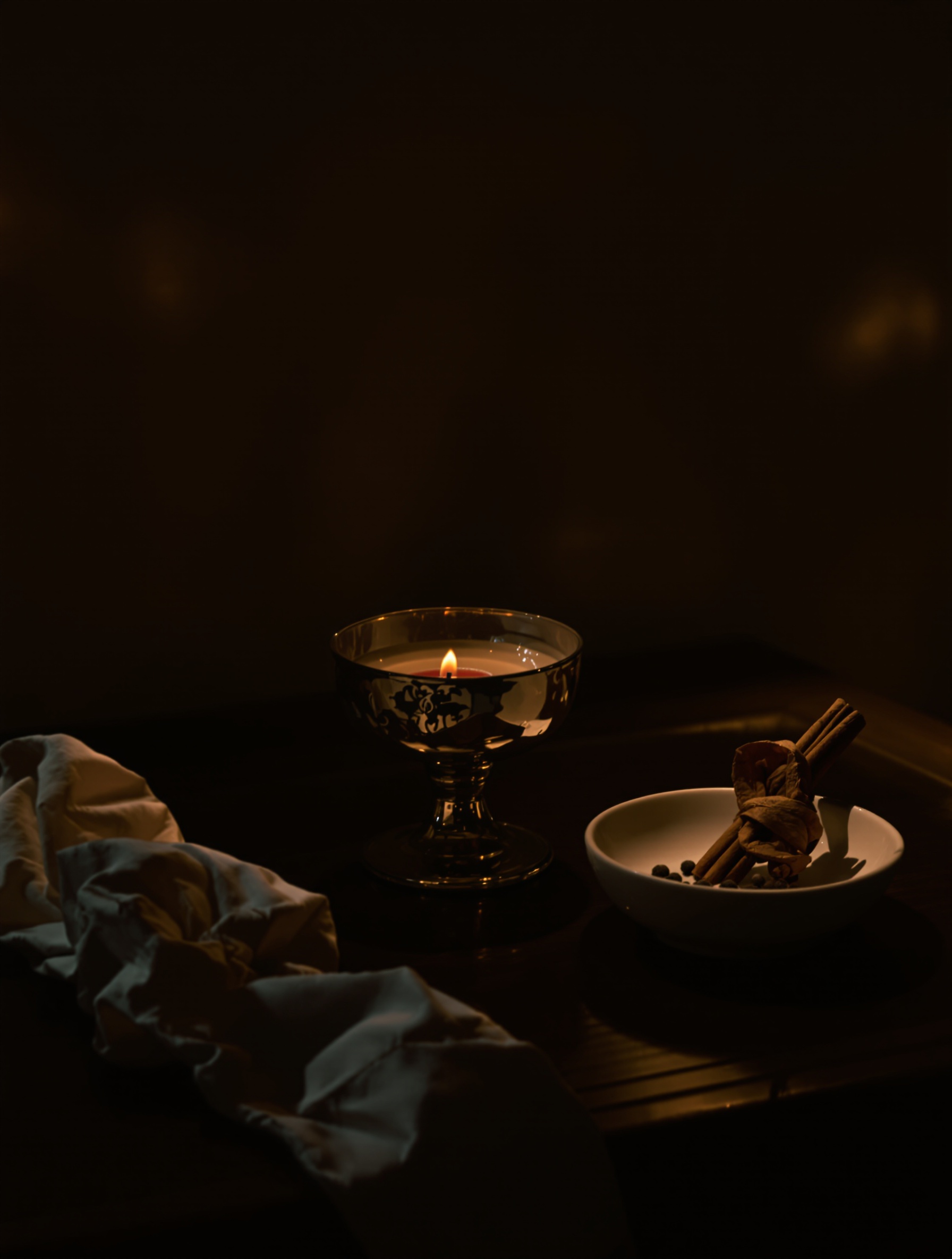 A tarnished candleholder, empty coupe glass, and cinnamon bark on a nightstand, a nighttime still life evoking Musc Ravageur.