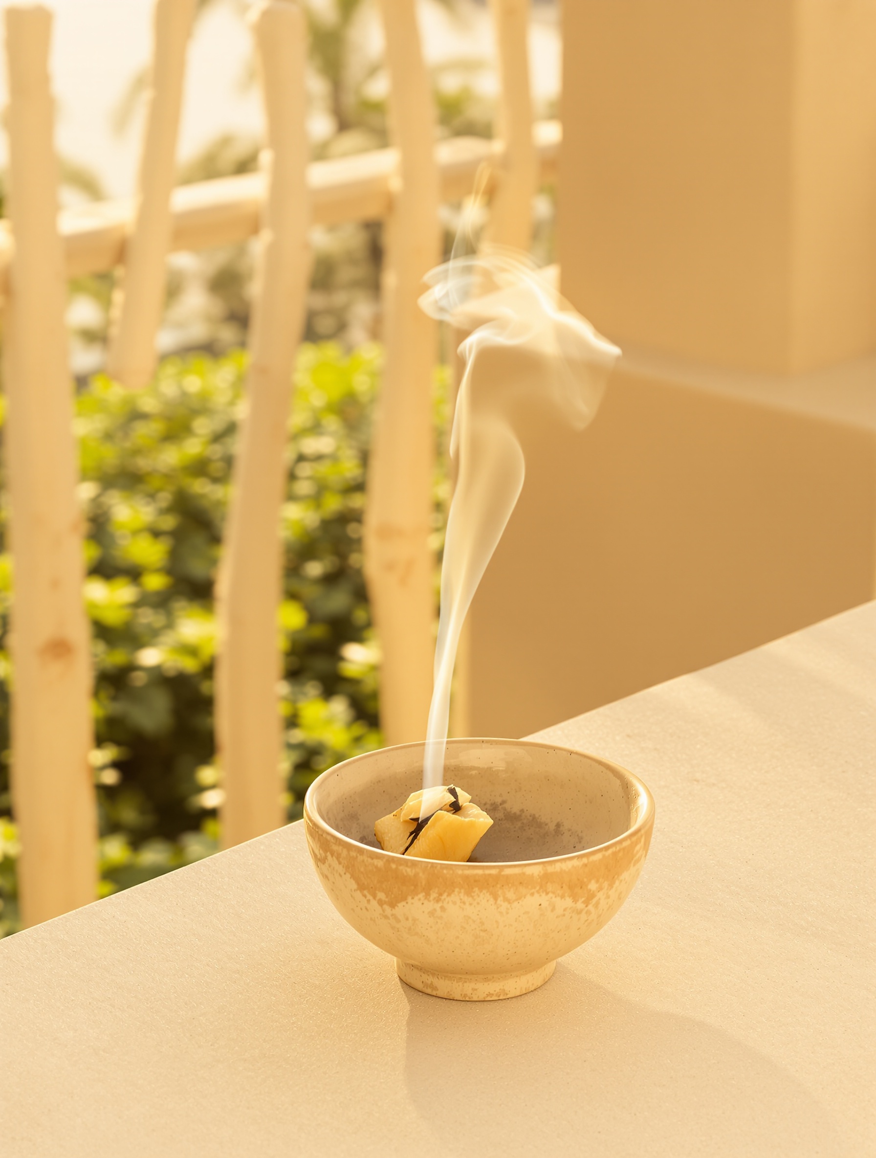 A thin thread of benzoin smoke bending in warm open air on a sun-warmed stone terrace, evoking Sand and Skin by Floraïku.