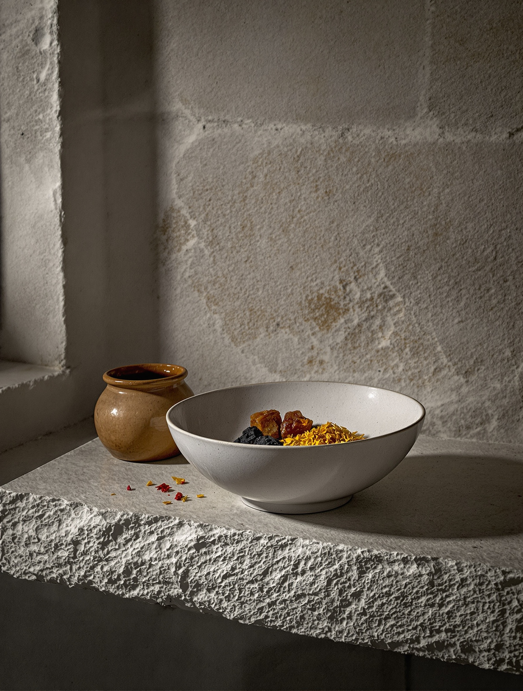 Raw dark resins and dried saffron in an unglazed ceramic bowl on a bare stone shelf, the material world of Amouage Outlands.