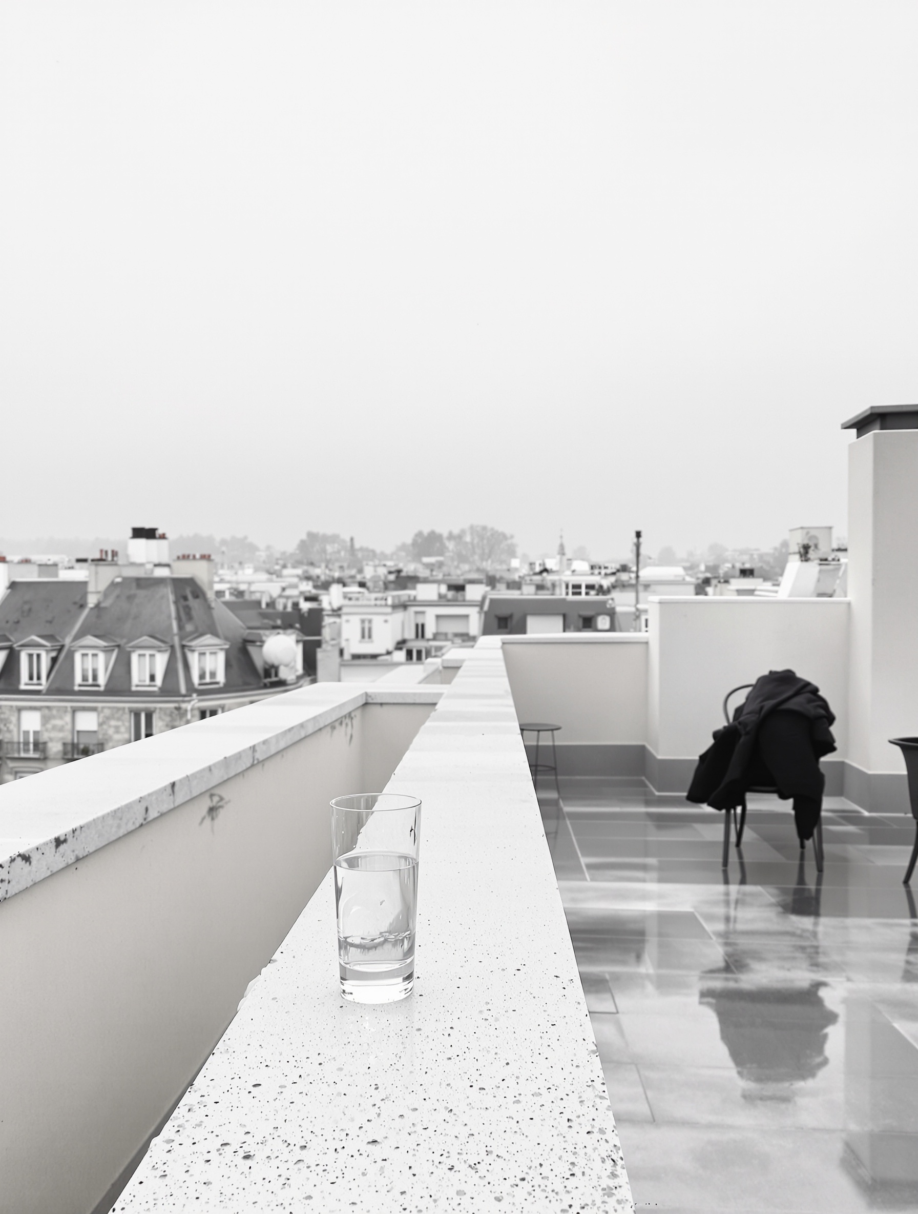 An empty rooftop terrace at grey dawn with an abandoned glass of water evoking the elevated solitude of Ganymede.