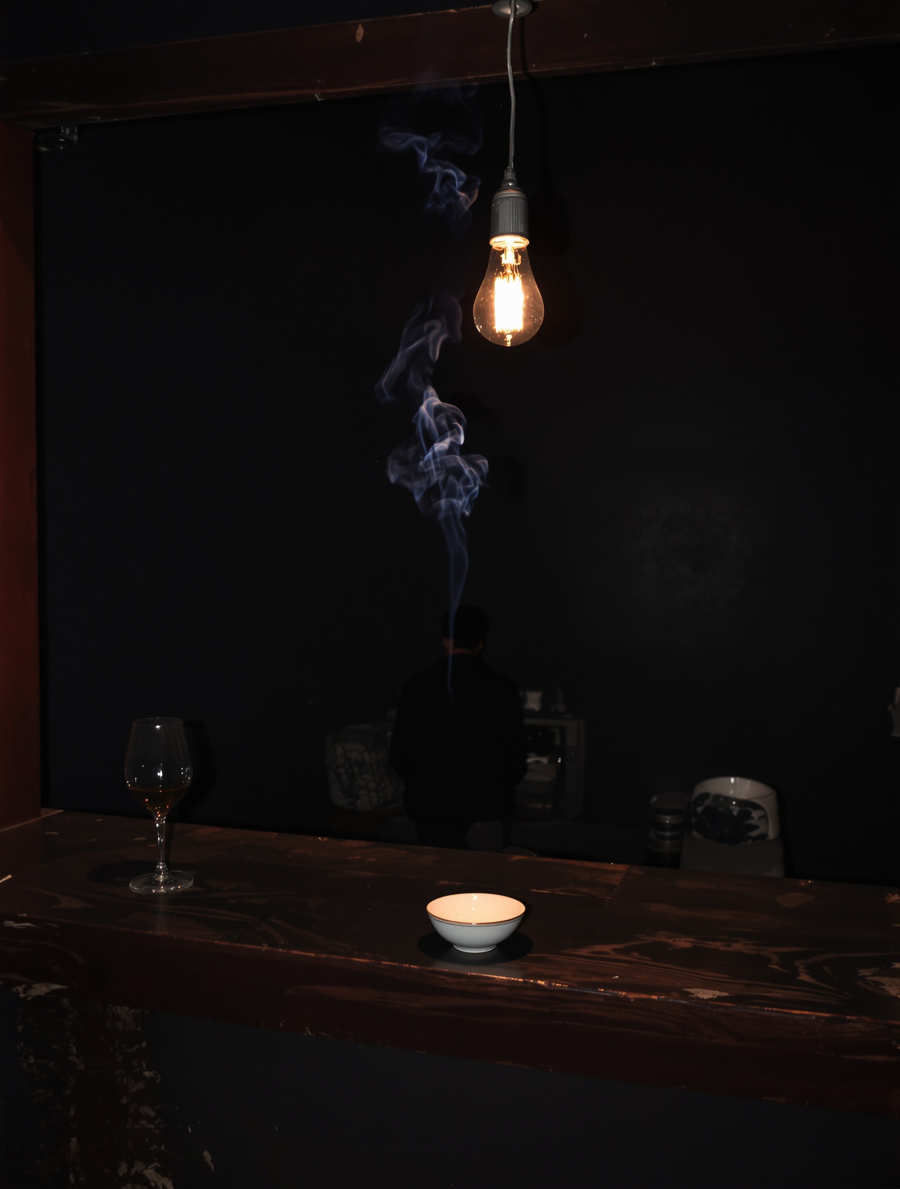 A solitary figure sits at a dim bar counter beneath a single glowing bulb, a thin ribbon of blue smoke rising through the warm amber light into bare dark walls.