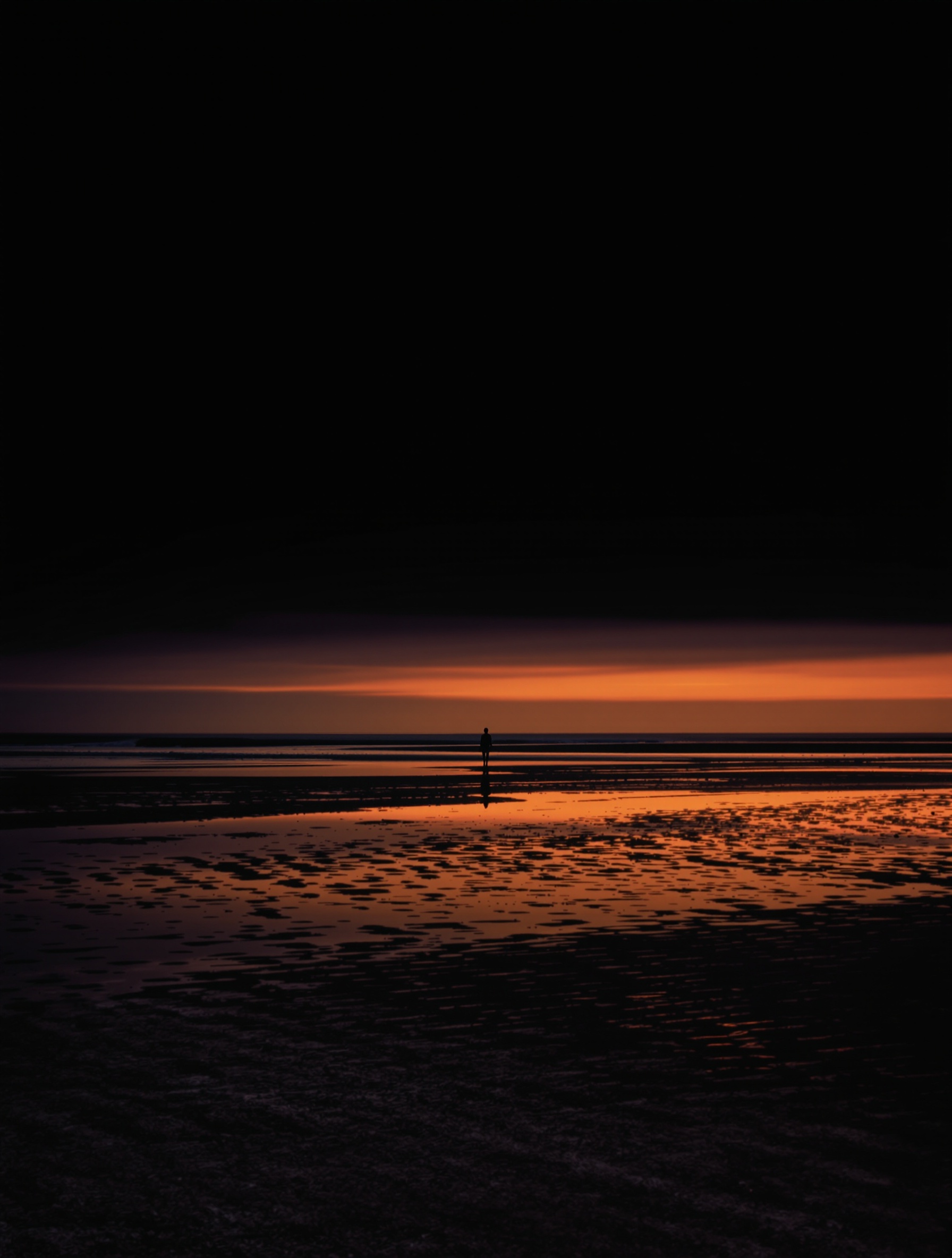 A solitary tiny figure standing at the waterline as the horizon turns from black to amber, evoking Risvelium's somatic homecoming after rupture.