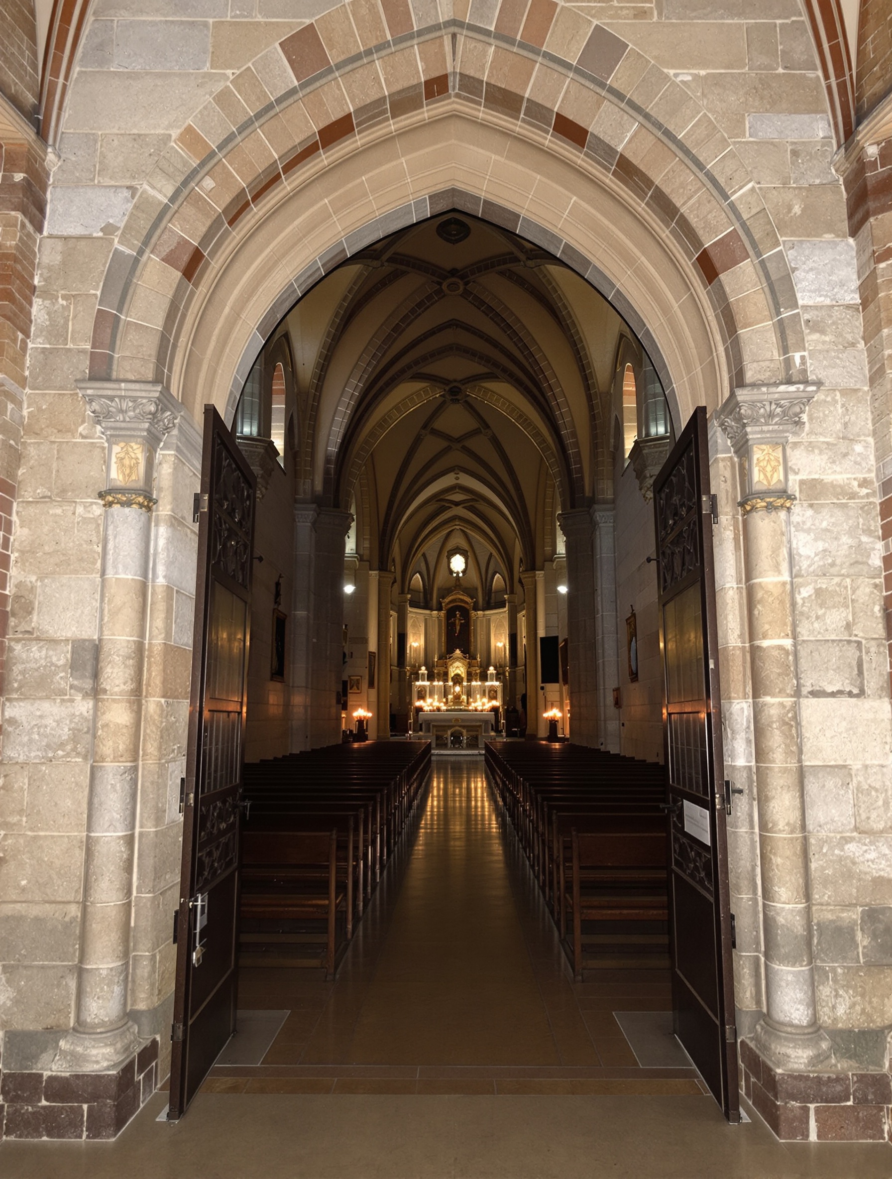 Empty Romanesque nave seen from the entrance, candlelight far in the distance, cold stone and incense haze, for Domus Numeni by Toskovat.