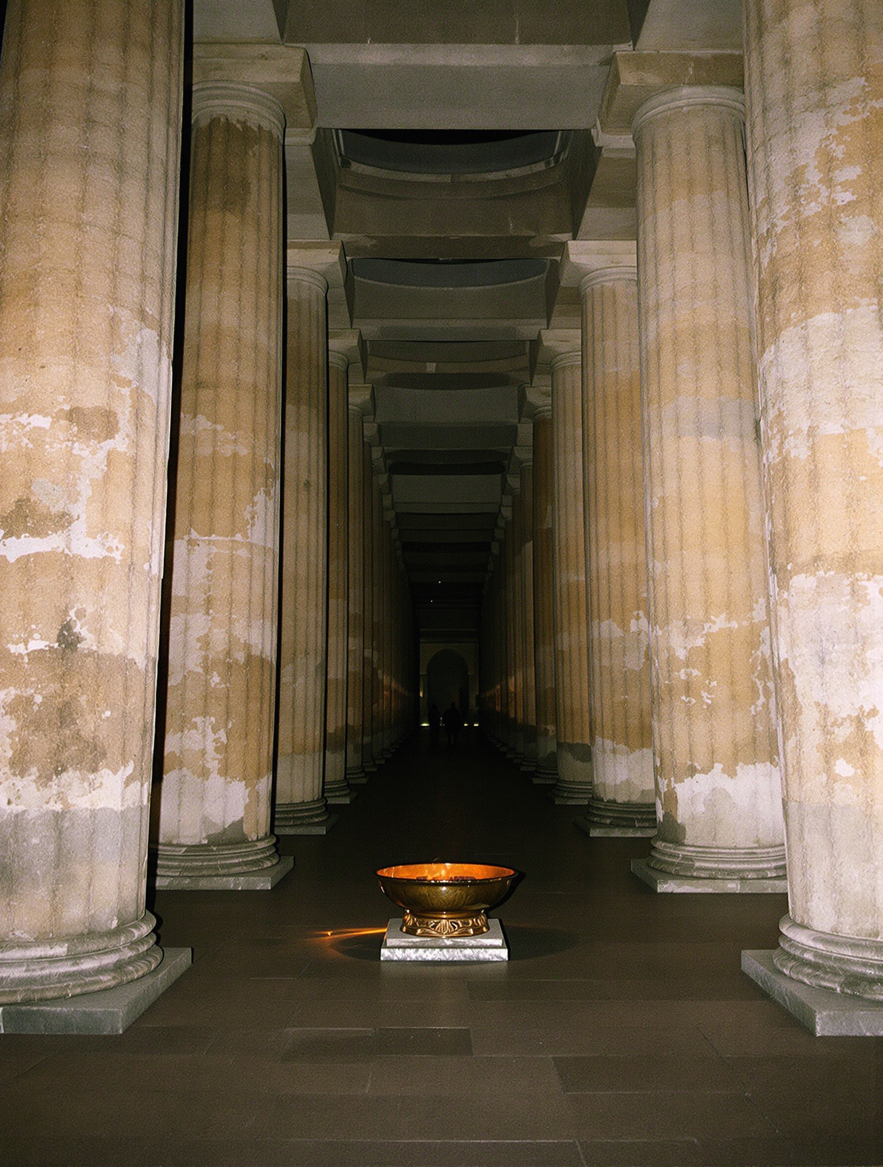 A real-film night photograph inside an ancient hypostyle hall where a single bronze fire bowl glows amber against massive stone columns fading into natural darkness.