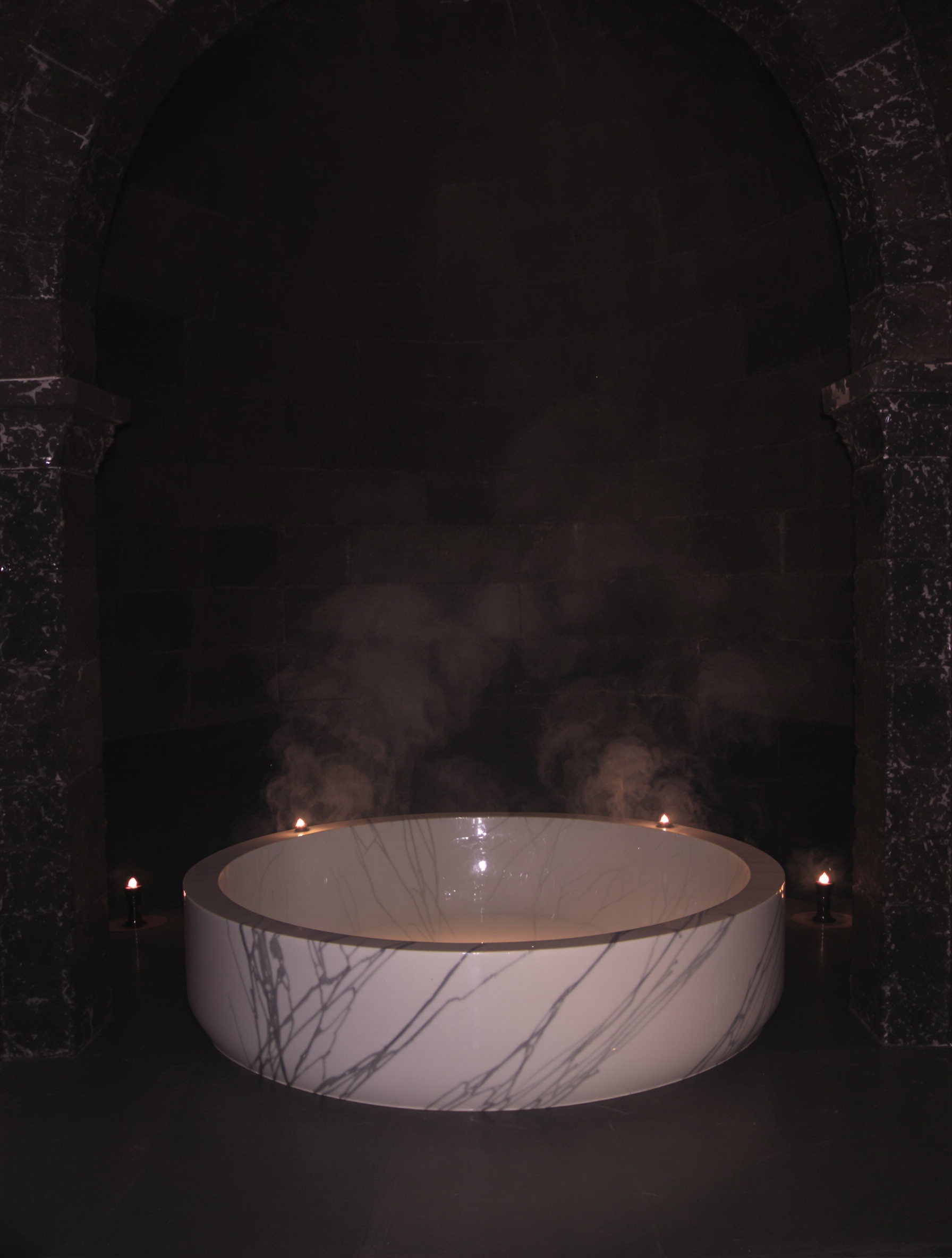 A candlelit ancient hammam with an empty marble basin and rising steam evokes the interior world of Jamaican Ambergris Purple Sultani.