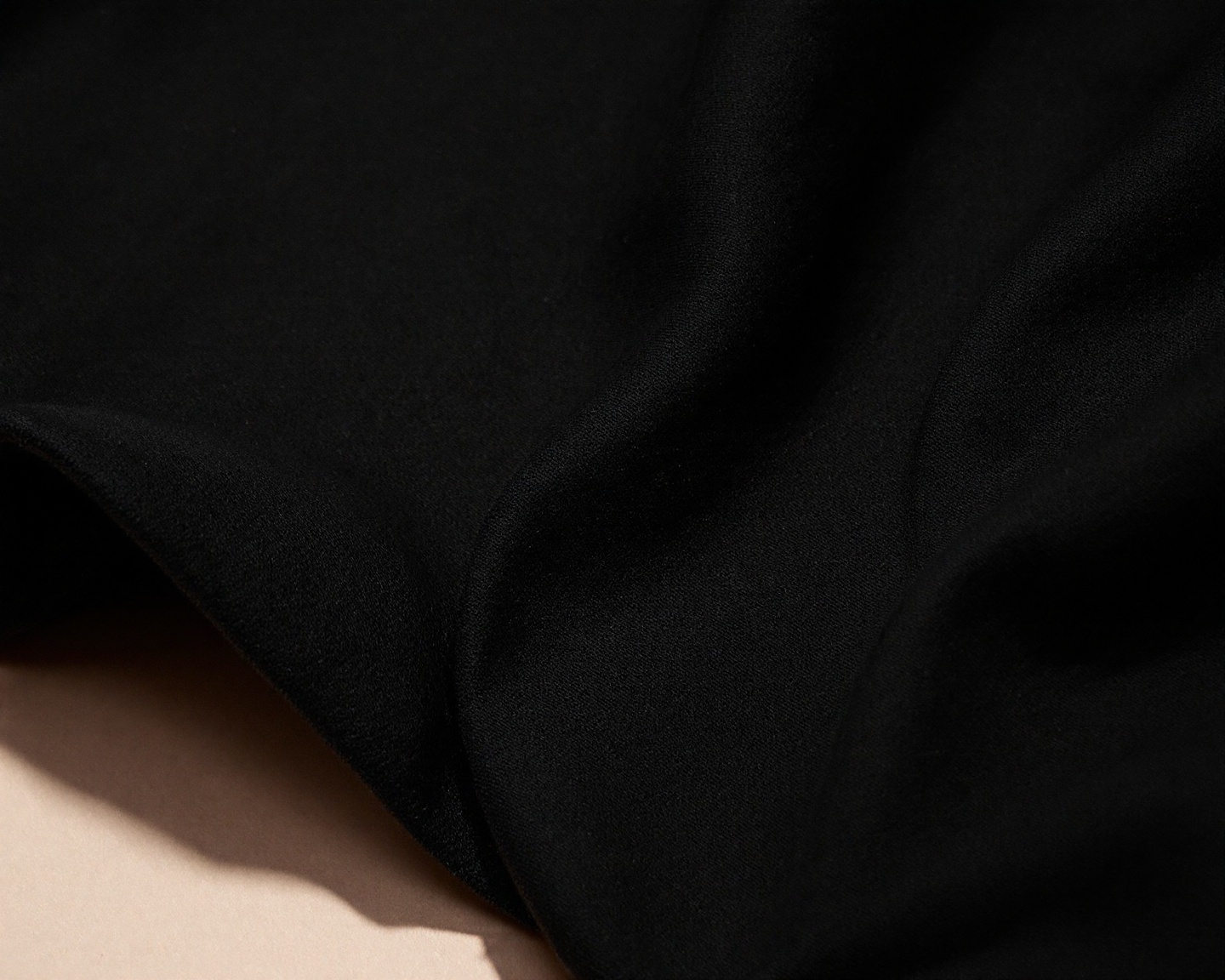 Close-up of black cotton fabric showing texture and drape, dramatic side lighting emphasising weave structure, minimal and abstract