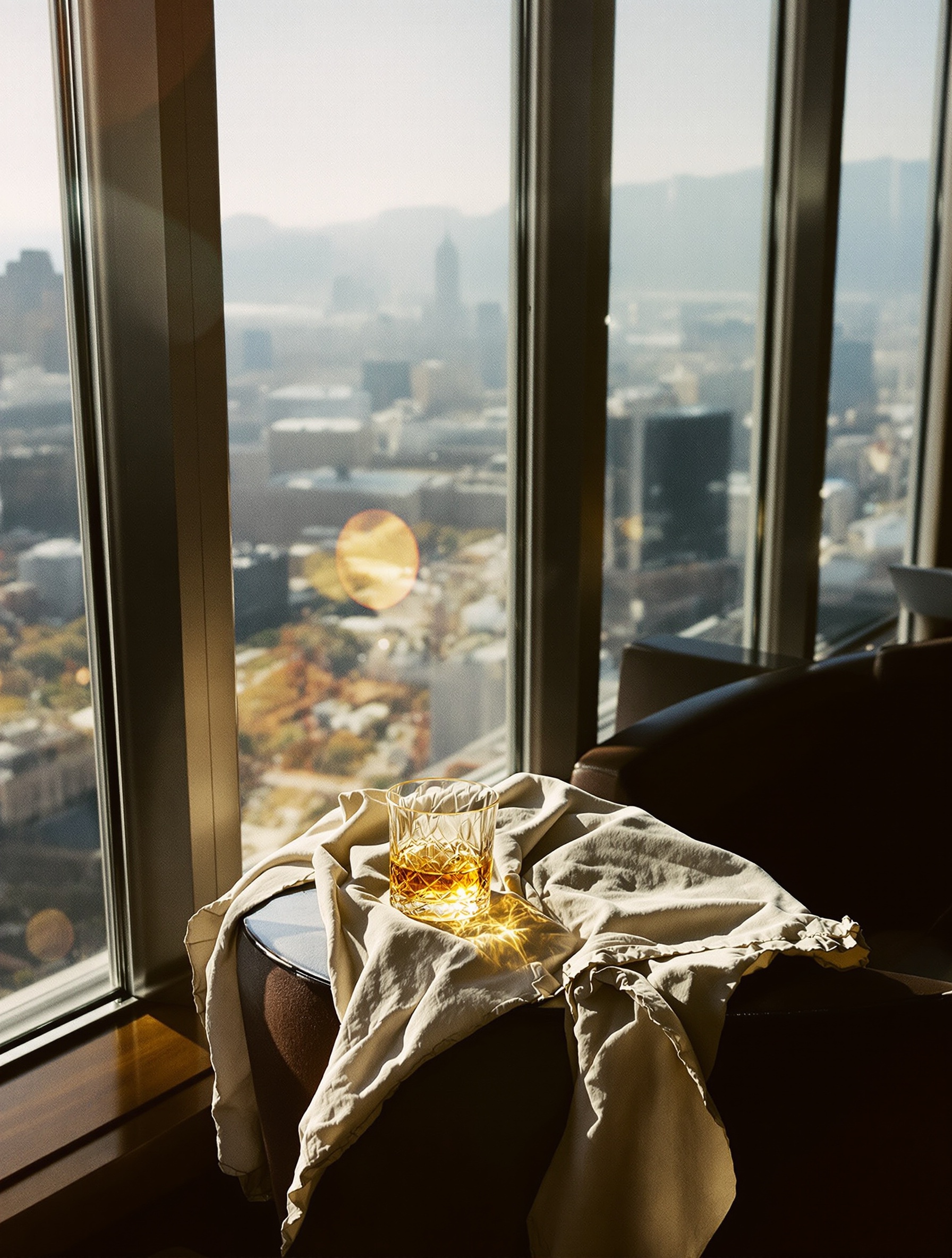 Abandoned crystal whiskey glass glowing amber in harsh late-afternoon penthouse light, shot on film.