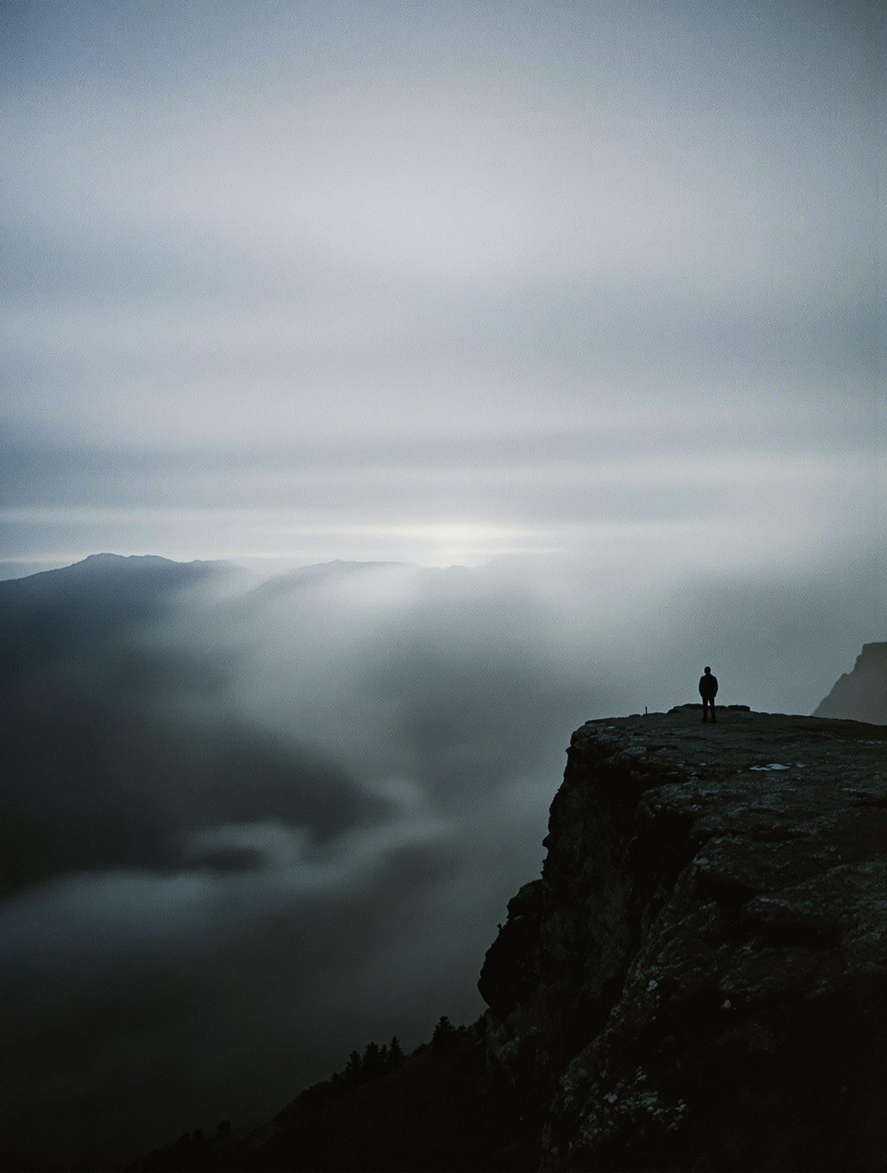 A solitary figure from behind on a misty mountain ridge bathed in cold moonlight on grainy film.