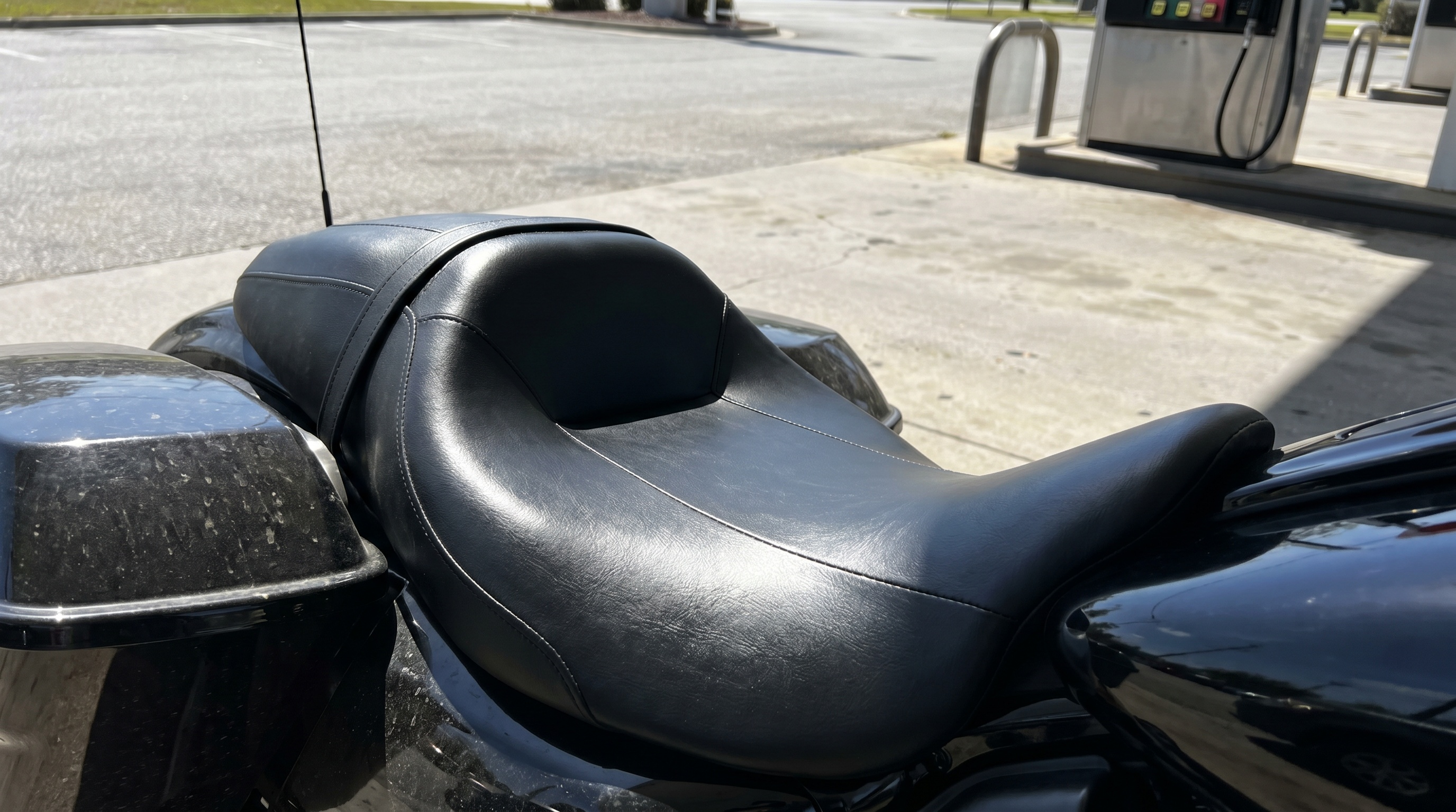 Close-up of a sun-heated black vinyl Harley seat surface showing heat buildup on a parked motorcycle