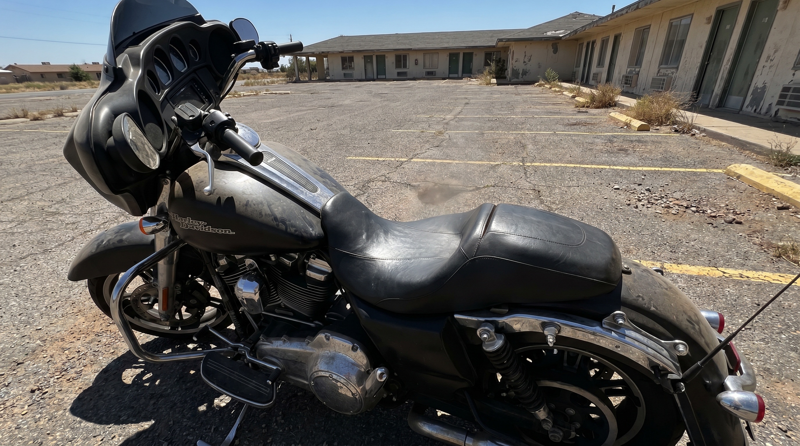 Close view of plain black factory vinyl motorcycle seat on a Harley bagger baking in harsh midday sun