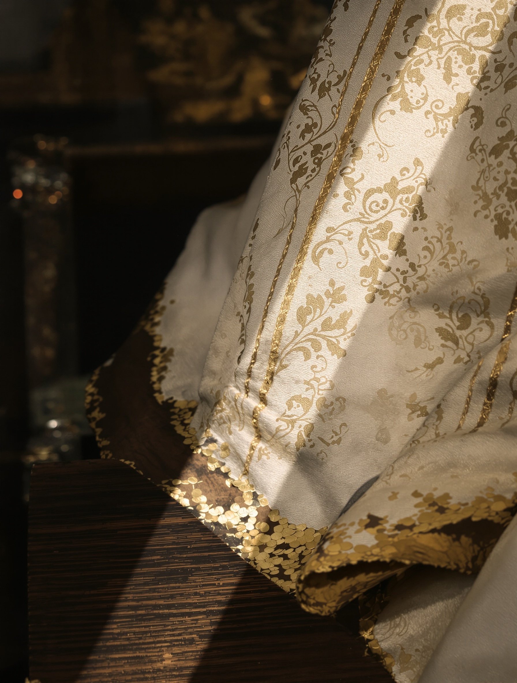 Extreme close-up of an ivory silk brocade vestment cope filmed with incense deposit and a dark labdanum smear at the hem, evoking the sacred material world of LAVS by Filippo Sorcinelli.