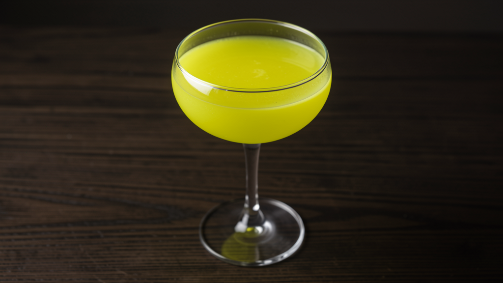 Nuclear Daiquiri in a chilled coupe glass, vivid yellow-green chartreuse color, on a dark wooden bar surface