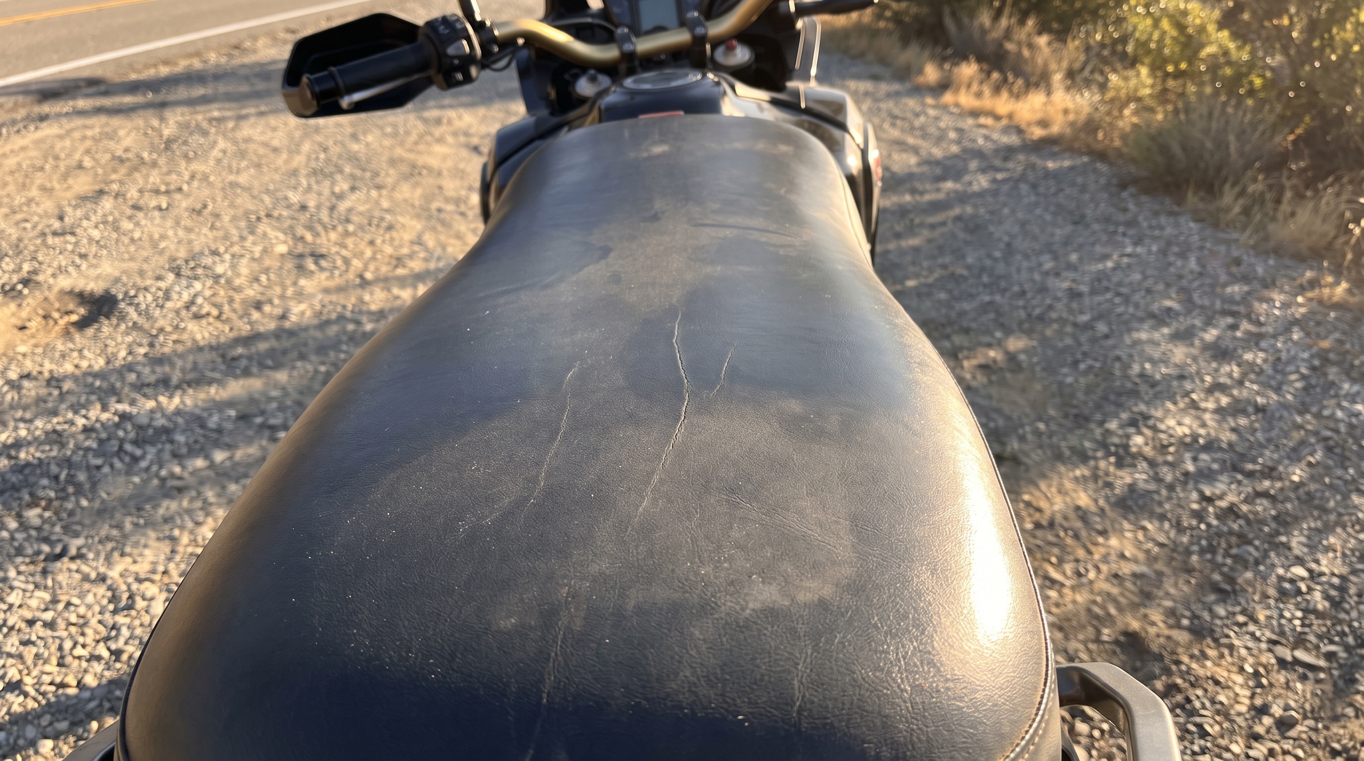 Close view of a Honda Africa Twin factory black vinyl seat in harsh afternoon sun showing heat buildup