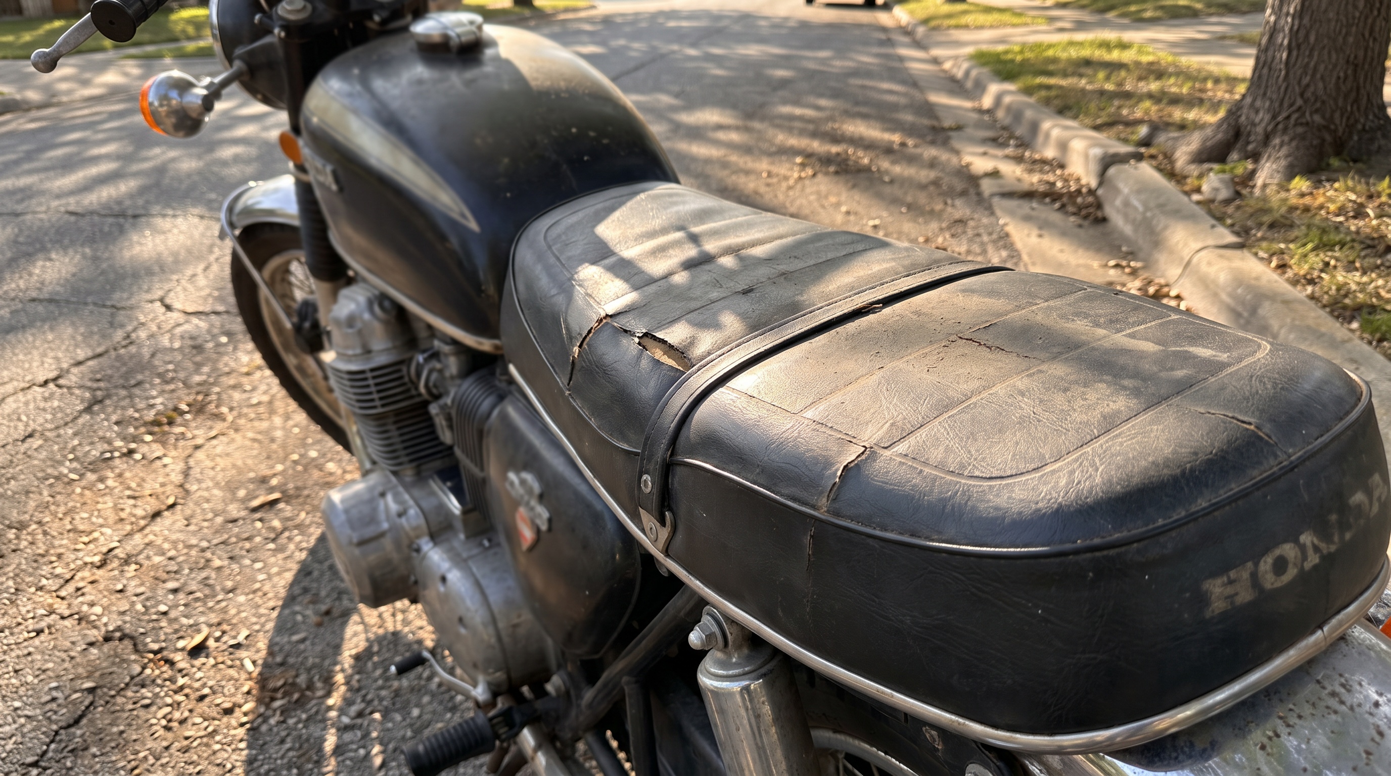 Close side view of a vintage Honda CB750 with a cracked worn factory vinyl seat trapping heat