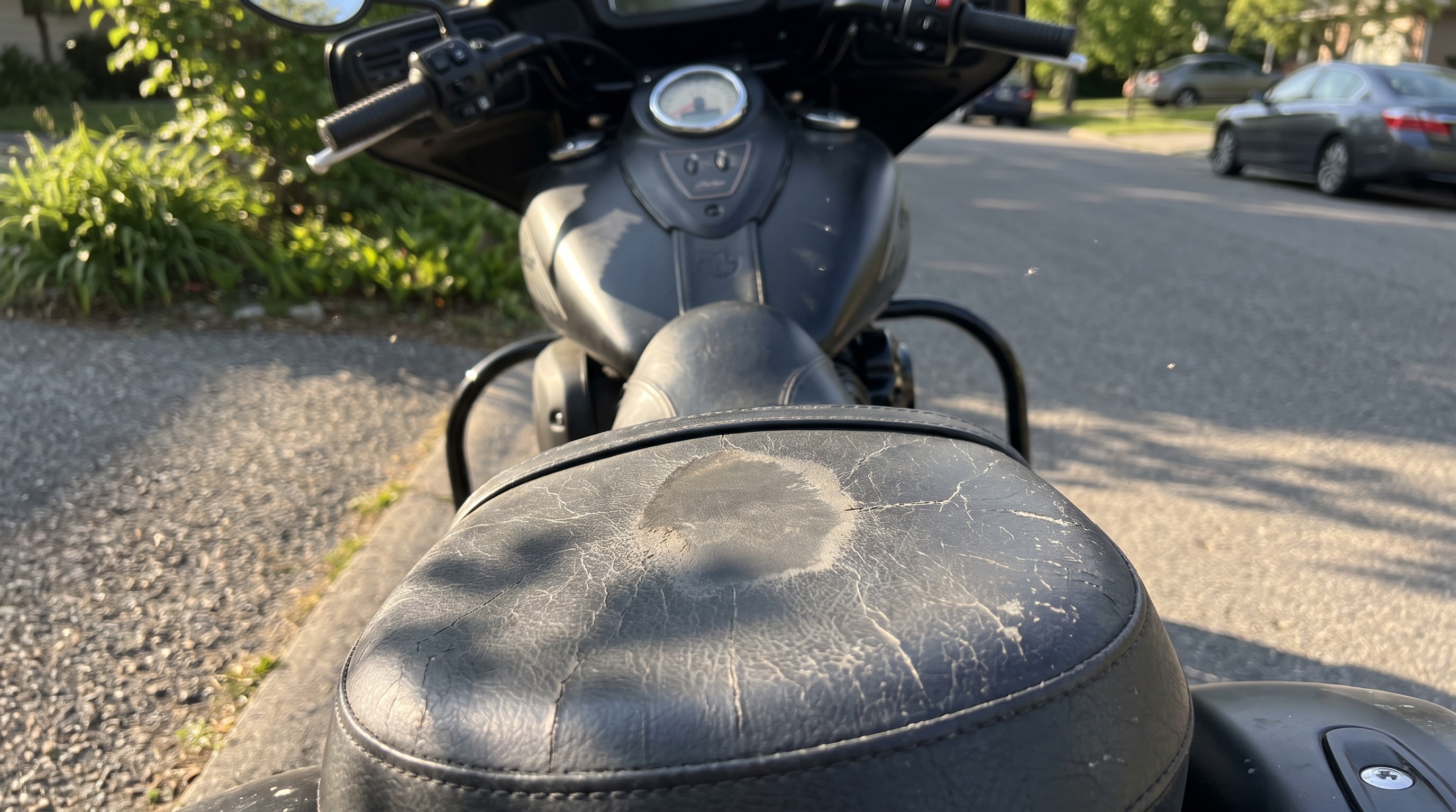 Cracked stock vinyl seat on an Indian touring cruiser showing sun damage in late afternoon open shade