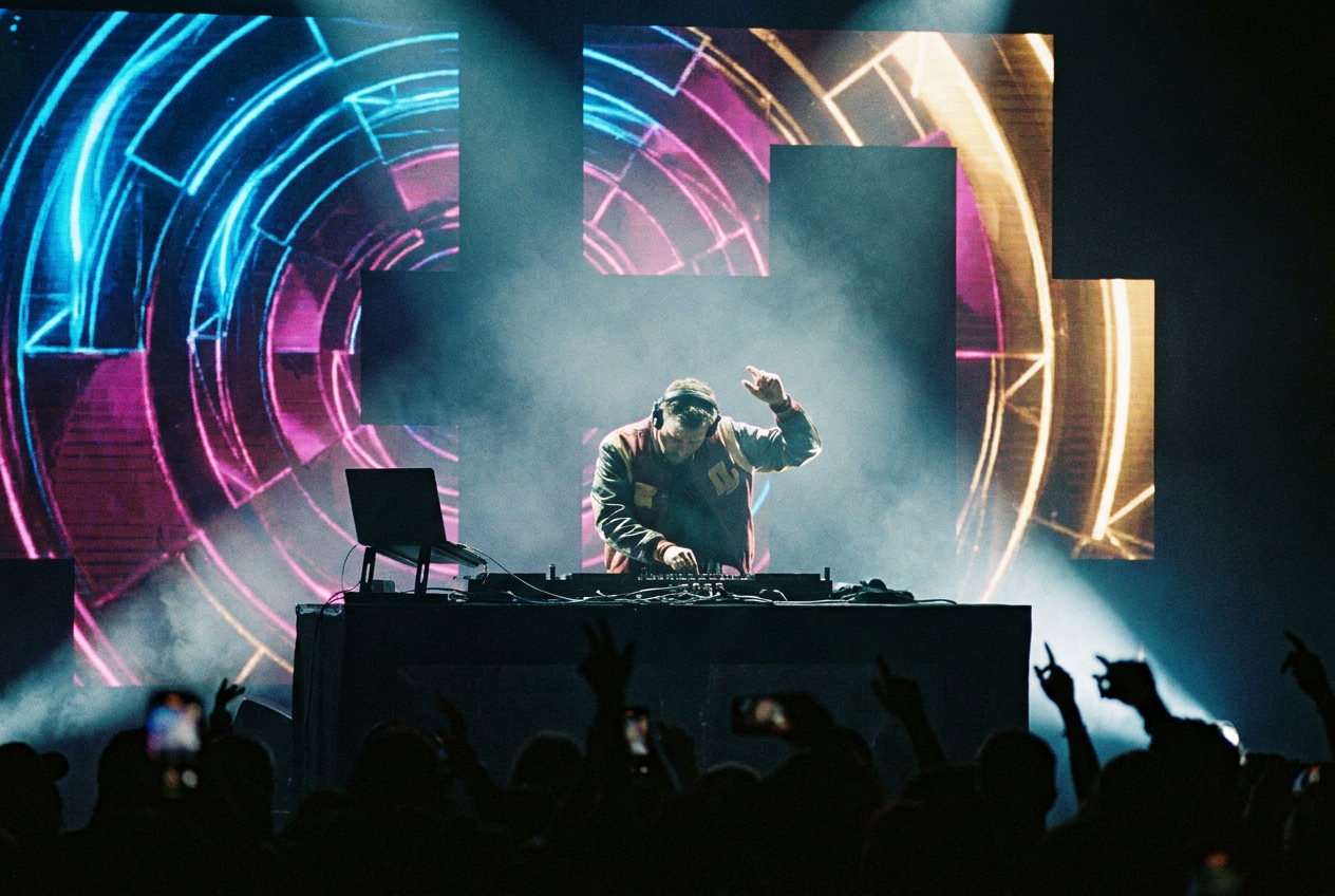 alt text: A DJ performing behind turntables with AI-generated abstract visuals projected on a large screen behind them, colorful geometric patterns pulsing to the music