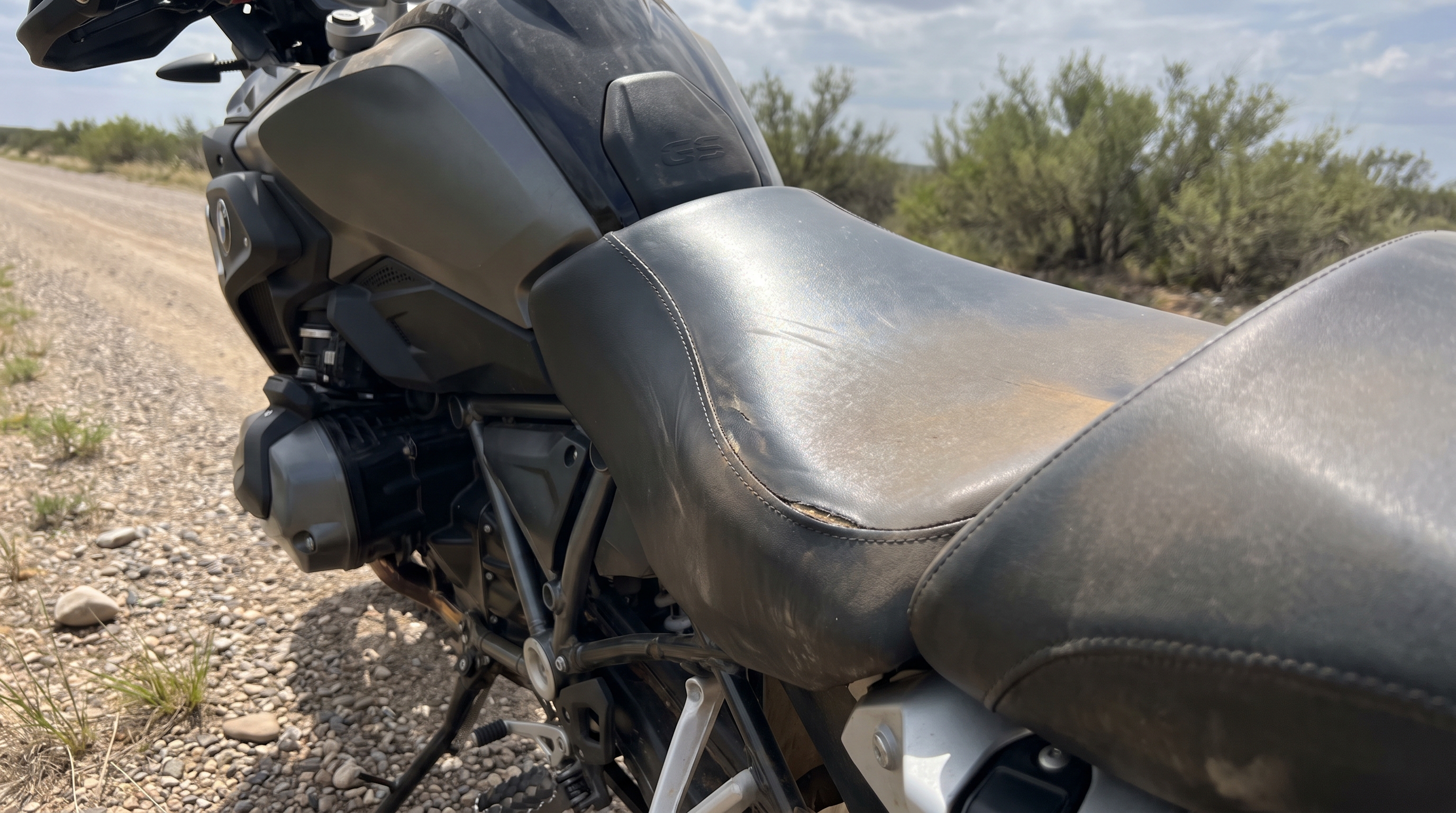 Close side view of a BMW R1250GS factory vinyl seat under bright sun showing heat buildup on plain black leather