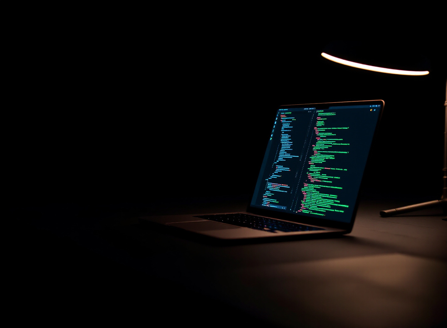 A developer's desk with a laptop showing code, on the right side of the frame