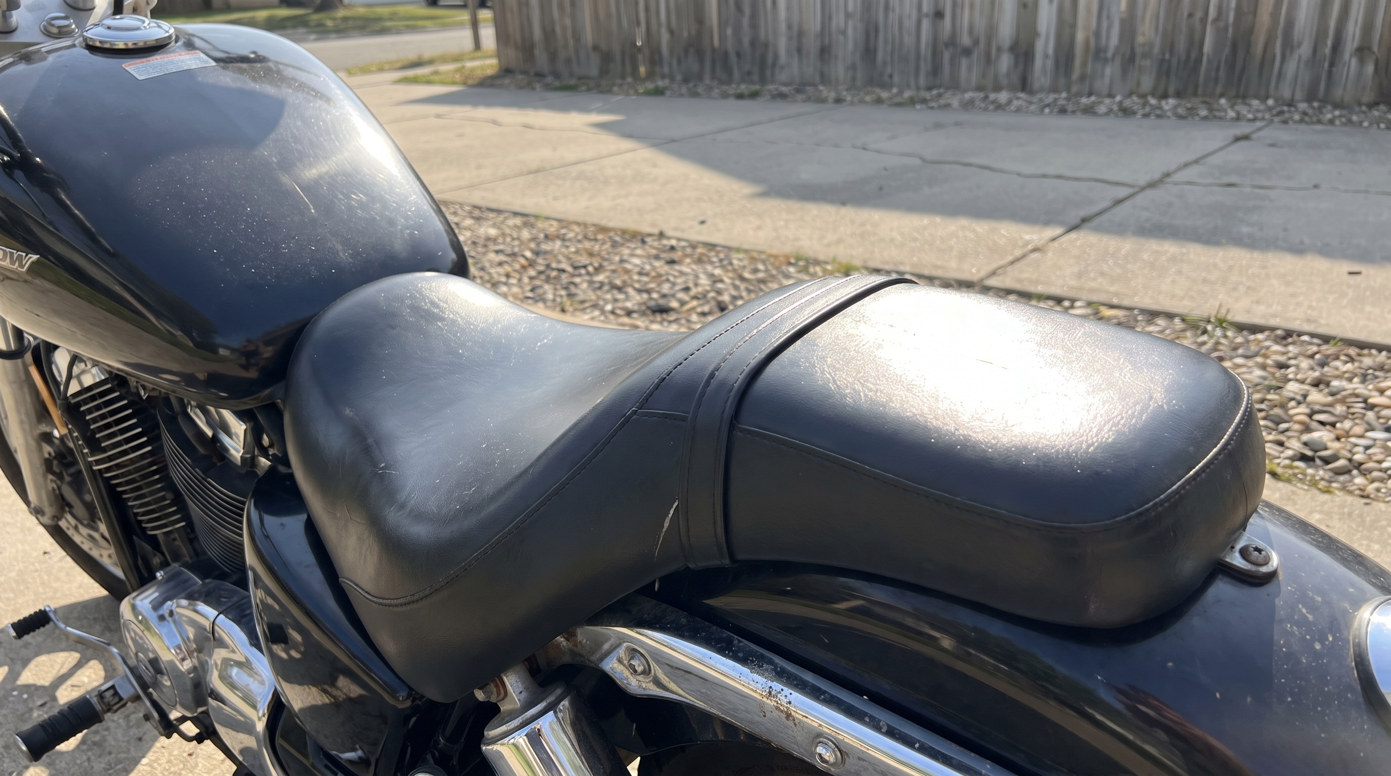 Close view of factory black vinyl motorcycle seat heating up in direct sunlight on a Honda cruiser