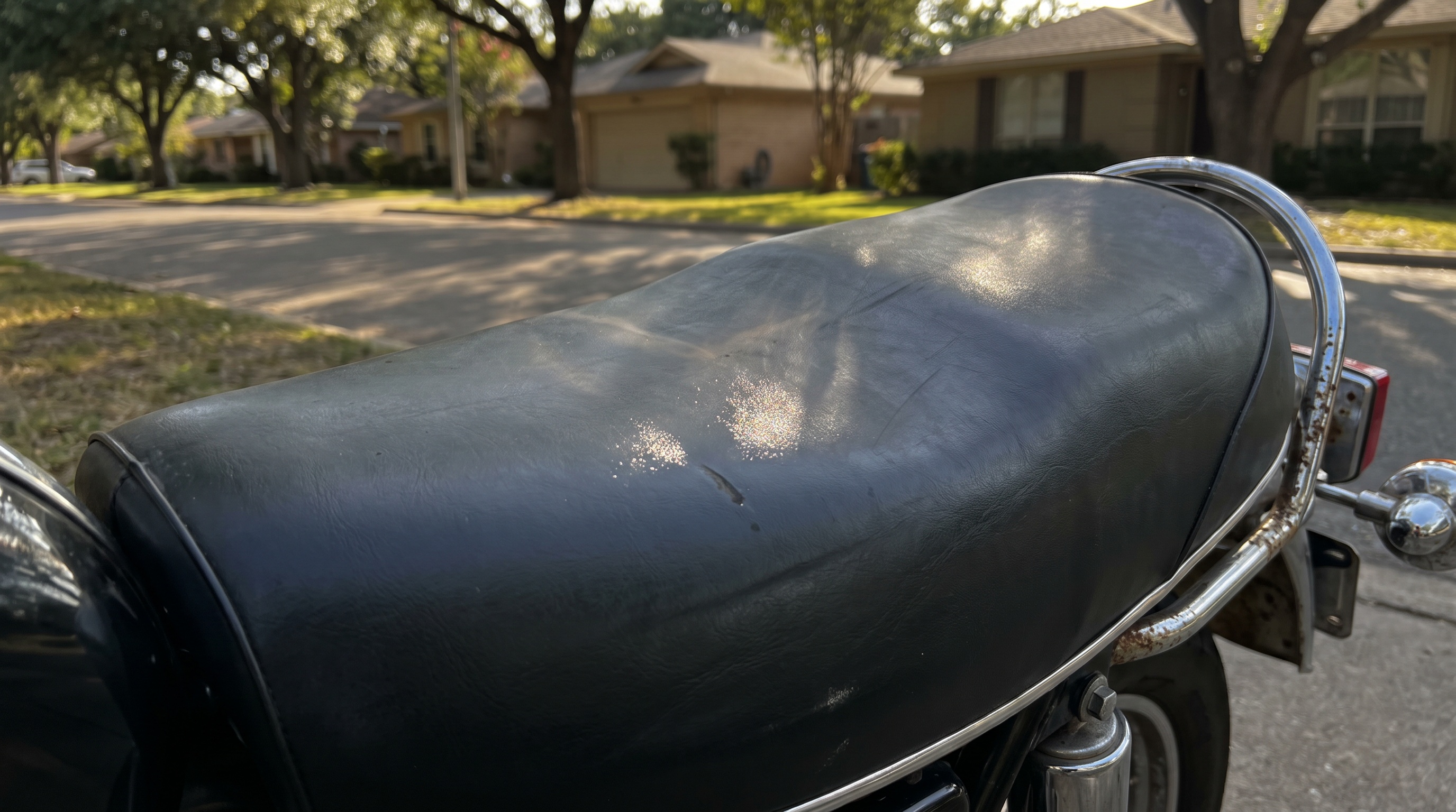 Close view of a Triumph Bonneville T120 stock black vinyl seat heating in late afternoon sun