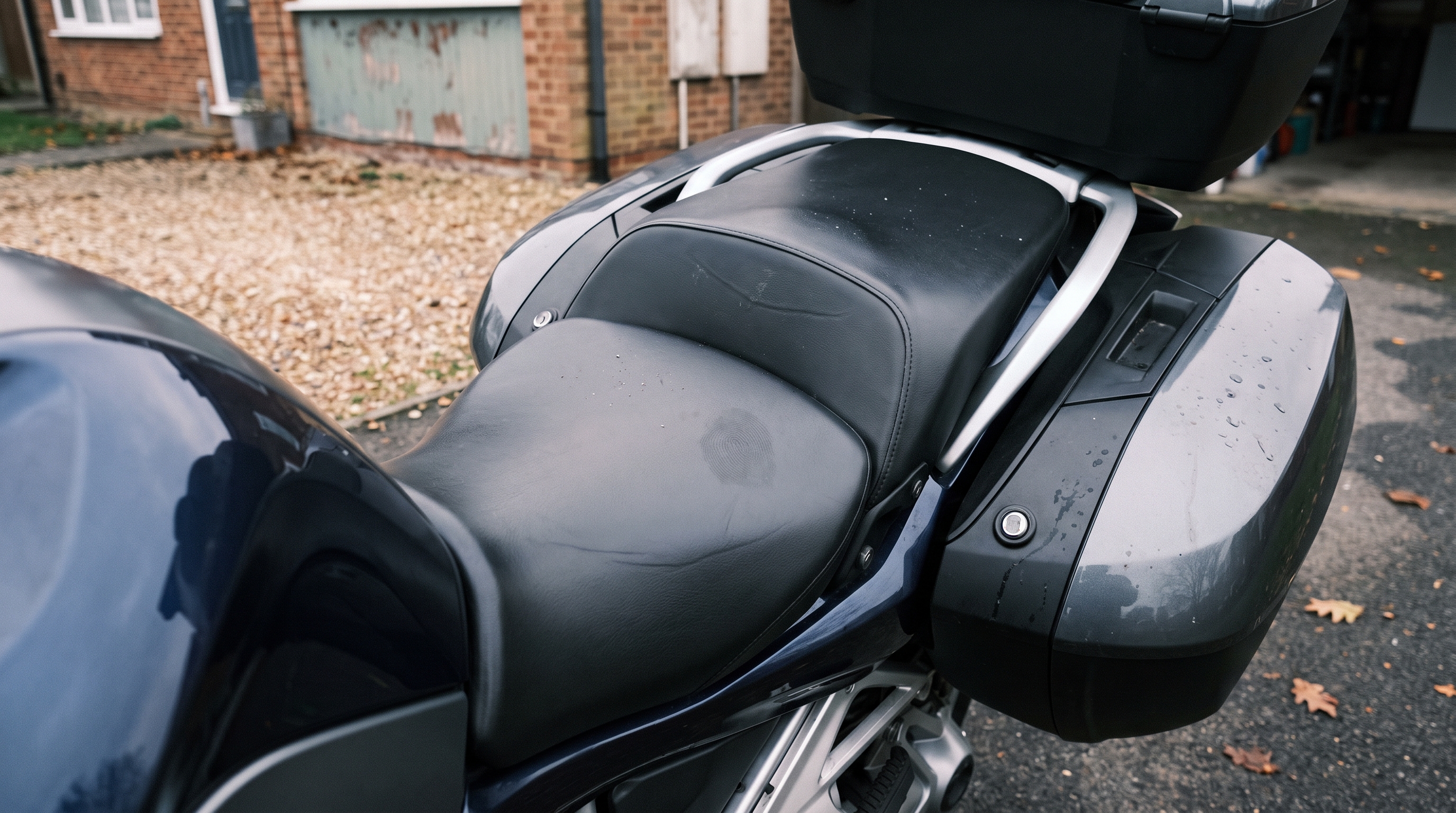 Close view of a BMW R1250RT hard saddlebag lid and factory vinyl seat showing sun and heat exposure