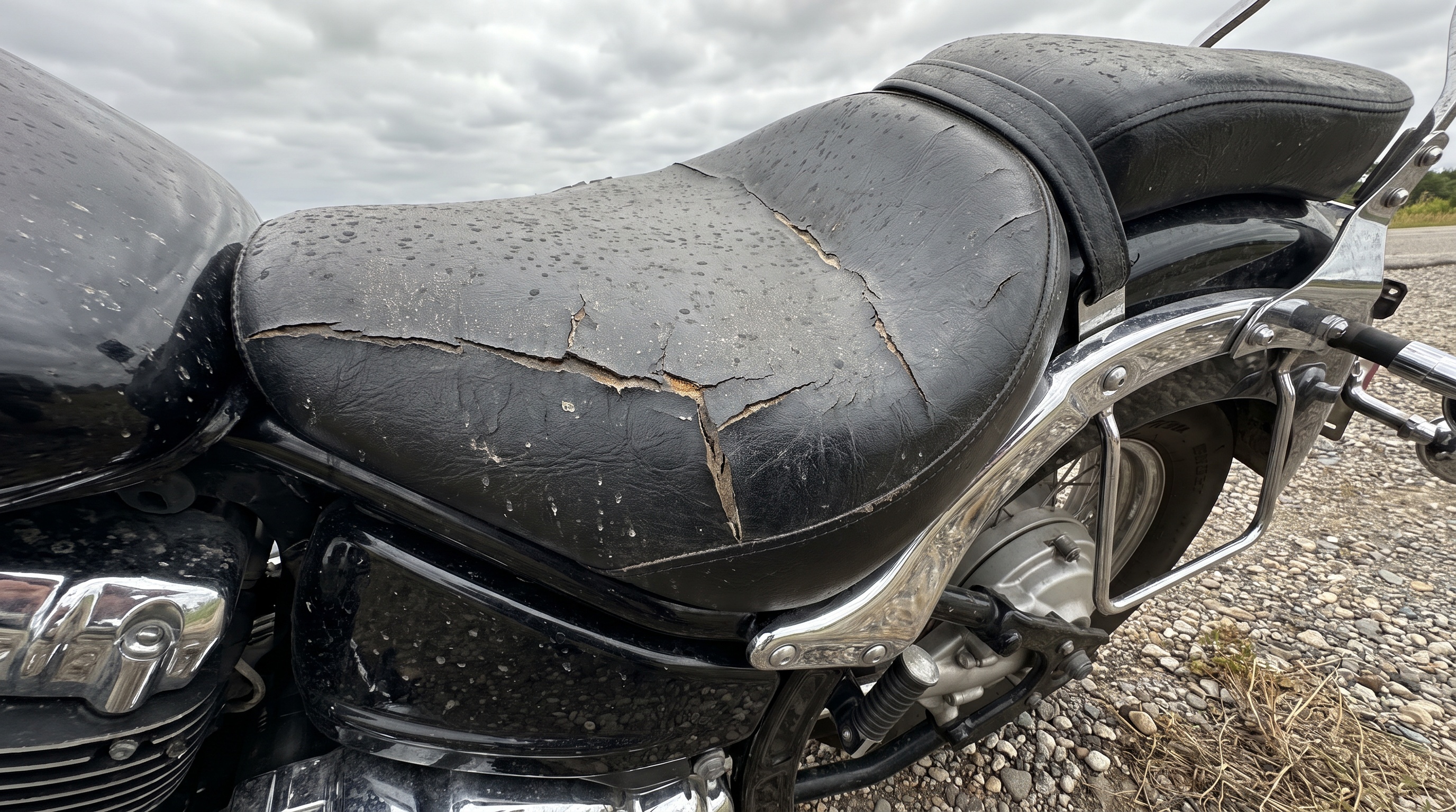 Close view of cracked factory vinyl seat on a metric cruiser explaining why old saddles trap heat
