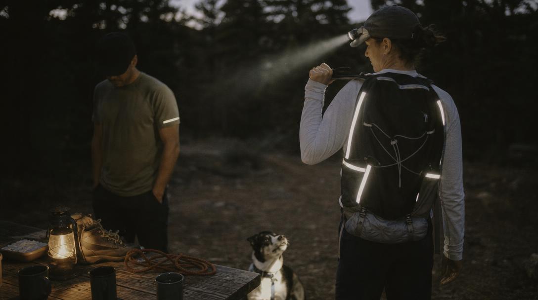 Hiker wearing reflective shirt near camp at dusk