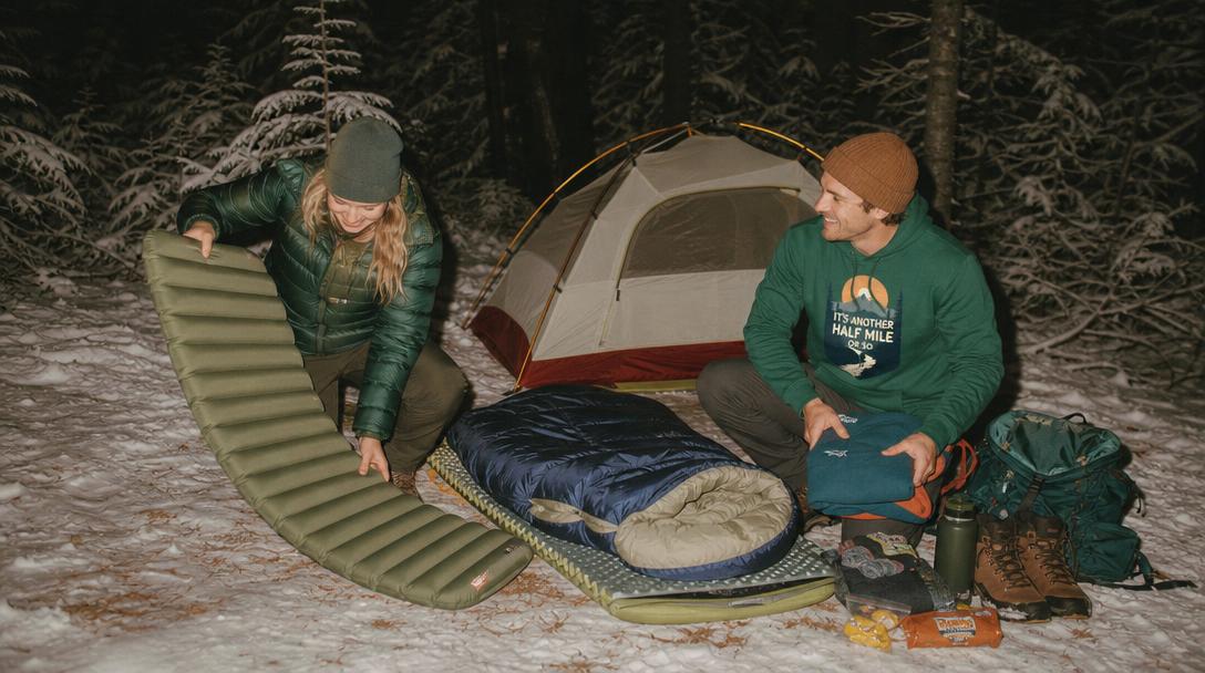 Various types of cold weather sleeping bags laying on ground